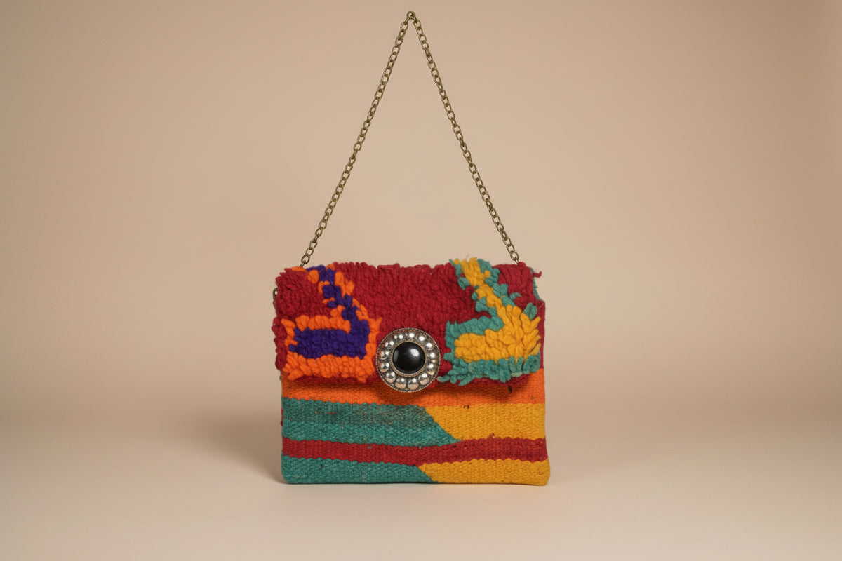 A small multicolor handbag with a textured, fuzzy flap and a chain strap, featuring a large decorative silver-tone button clasp on a light beige background.