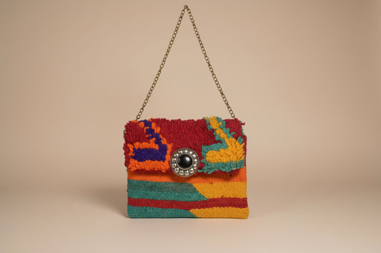 A small multicolor handbag with a textured, fuzzy flap and a chain strap, featuring a large decorative silver-tone button clasp on a light beige background.